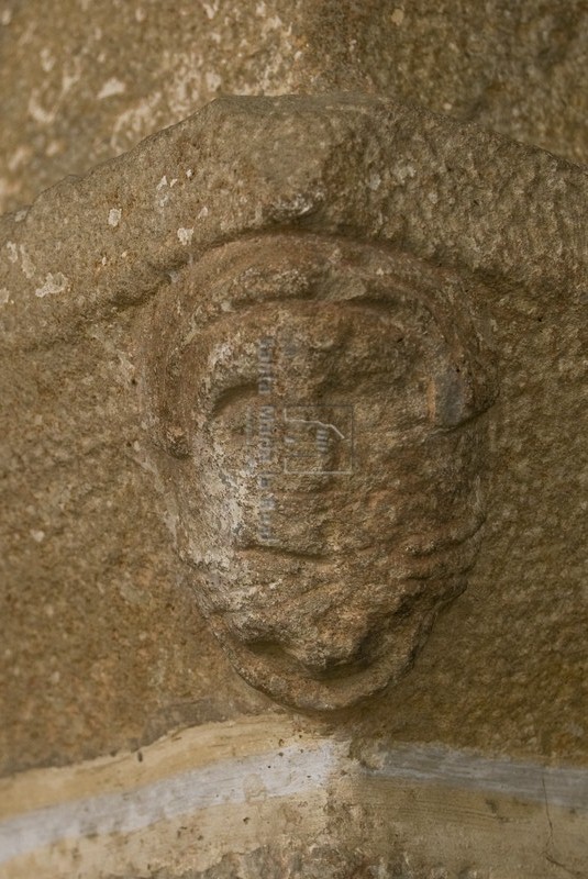 Cabeza de personaje barbado sonriendo en la imposta izquierda de la portada