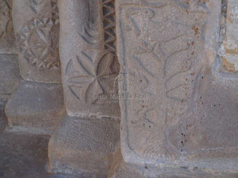 Detalle de la basa de la portada con flores hexapétalas y un árbol con una paloma en su copa