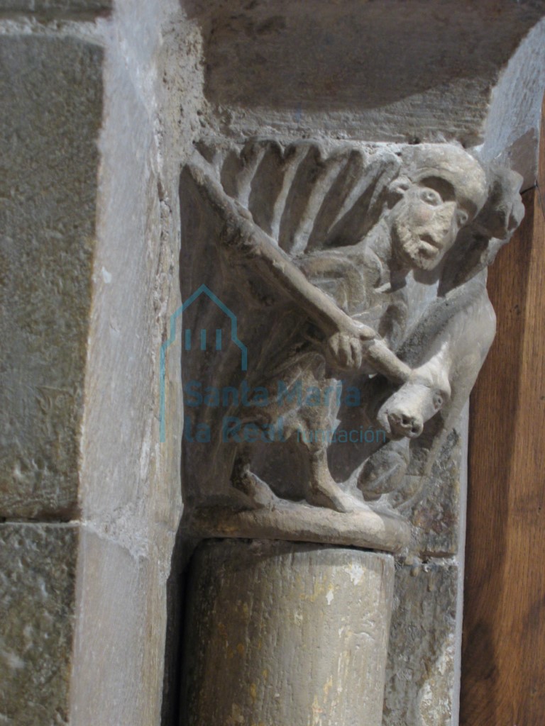 Capitel del arco de comunicación entre la capilla mayor y la capilla del Evangelio. Hombre que alancea un jabalí bajo dos volutas