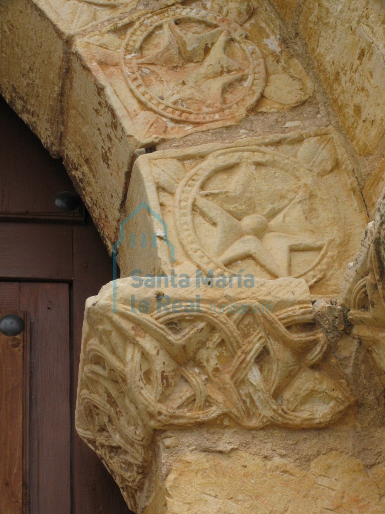 Detalle de las dovelas del arco decoradas con flores de seis pétalos dentro de clípeos perlados y con cuatro hojitas repartidas en cada esquina de la dovela. Y del cimacio decorado con estrellas de cuatro puntas enmarcadas en círculos