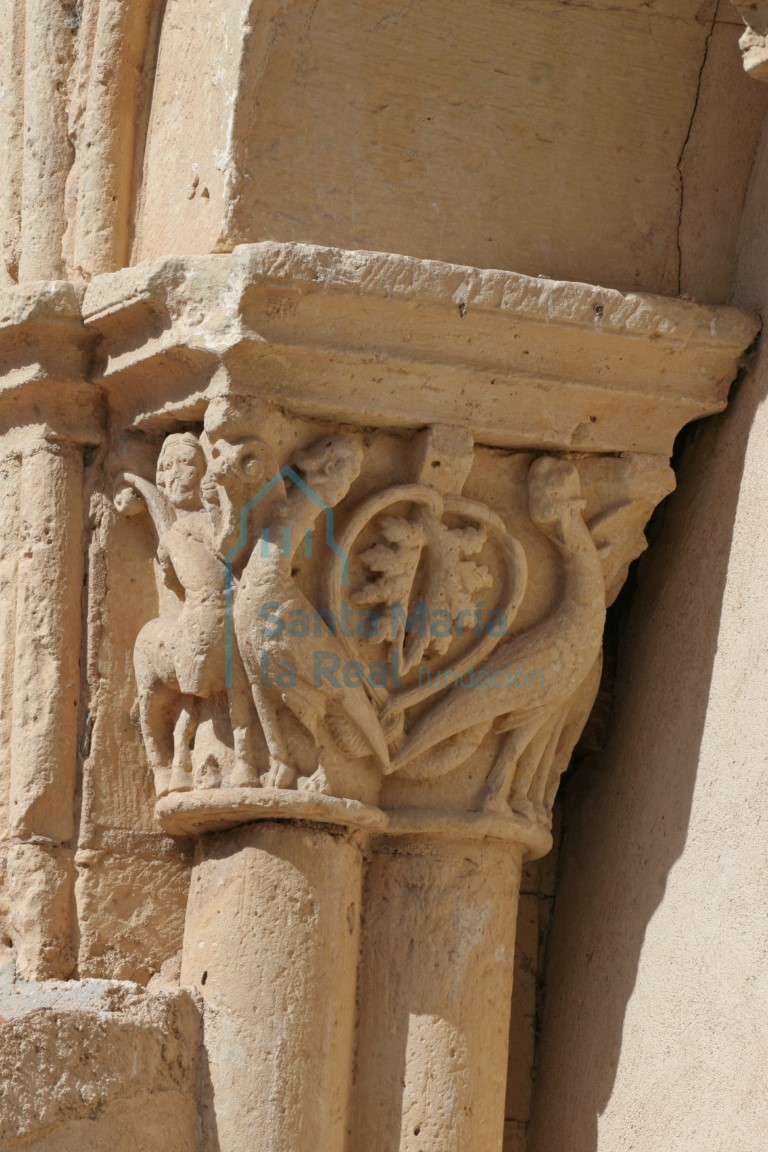 Capitel de la galería porticada figurada con ornamento en los ángulos de sendos centauros-sagitario de cabellera rematada en brotes vegetales que tensan sus arcos hacia estilizadas arpías de largo cuello vuelto