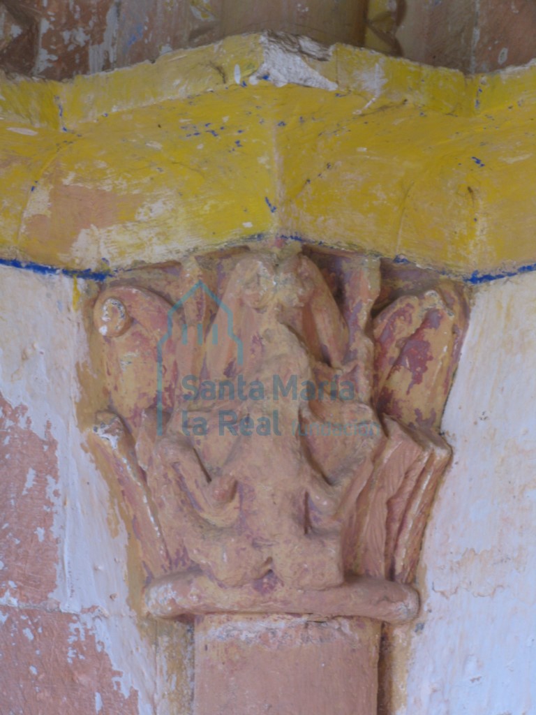 Capitel de temática mitológica en el que se prepresenta un fondo vegetal con un deteriorada sirena de doble cola sin cabeza. En la portada