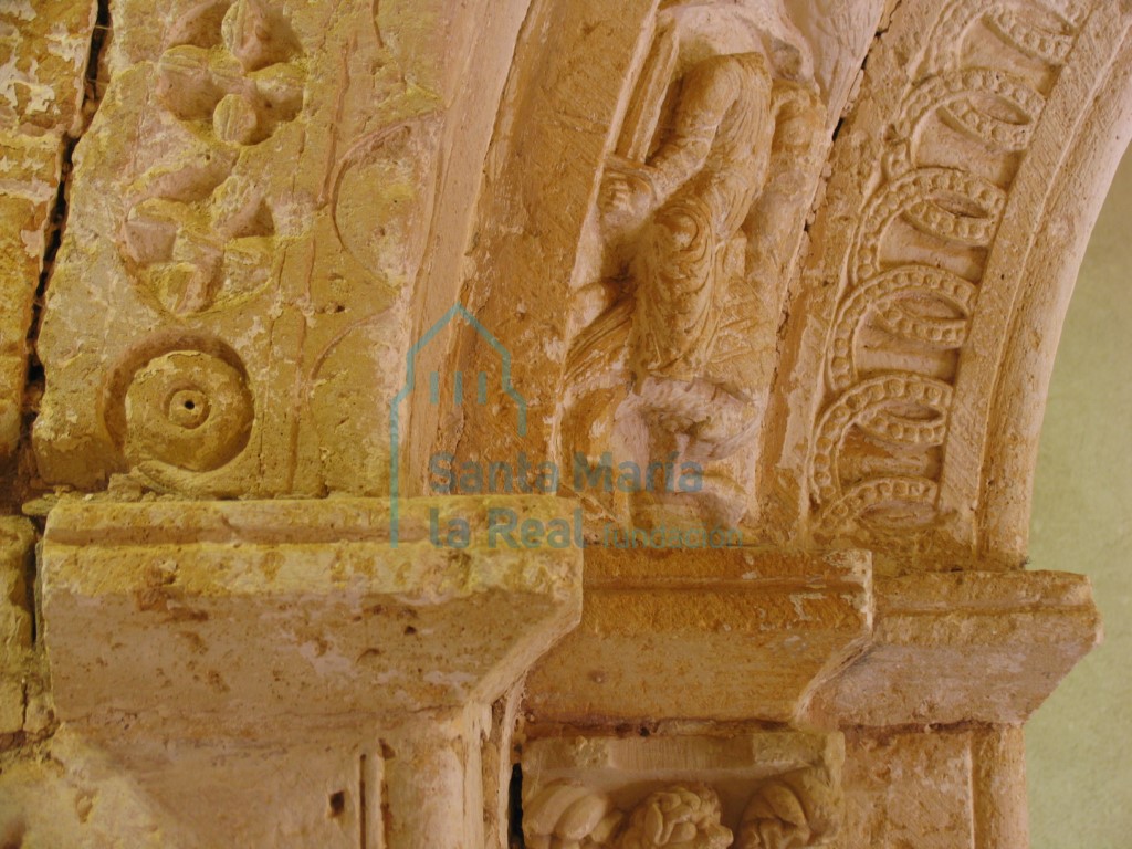 Detalle de la portada, en el que se puede ver la sencilla decoración de bezantes con tetrapétalas inscritas en círculos, tallados a bisel en el salmer de la izquierda Detalle de la portada, en el que se puede ver la sencilla decoración de bezantes con tetrapétalas inscritas en círculos, tallados a bisel en el salmer de la izquierda