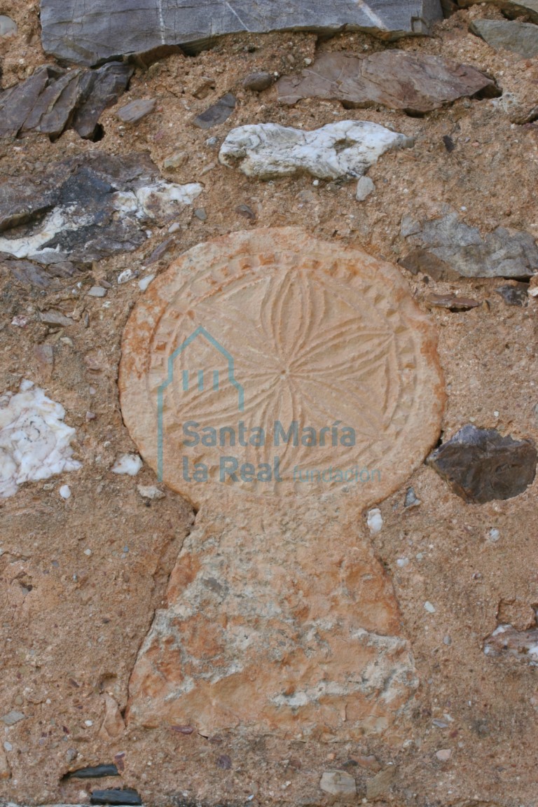 Estela con flor hexapétala inscrita en un círculo, reaprovechada en el muro de la espadaña