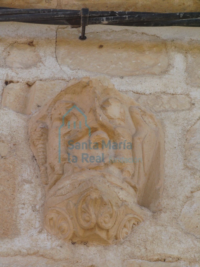 Capitel reutilizado en el muro norte sobre la portada. Un pájaro, un árbol y dos figuras humanas que parecen luchar