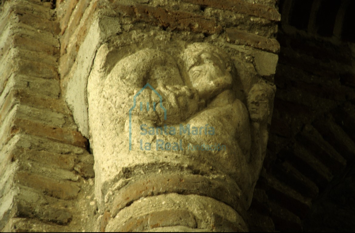 Capitel del arco triunfal en el lado del evangelio. Figura humana, a cuyo cuyo cuello se lanza un dragón y a espaldas del personaje otra cabecita masculina