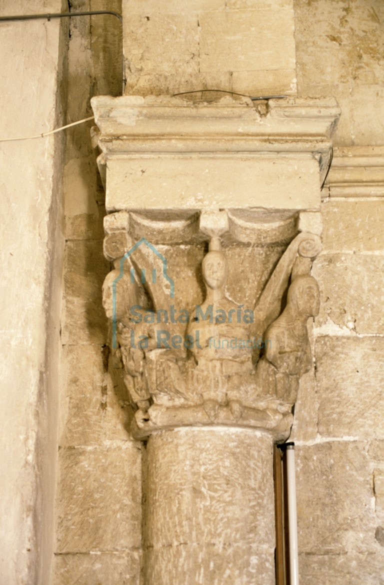 Capitel del lado del evangelio en el arco triunfal del absidiolo sur. Tres figuras femeninas sedentes, vestidas con túnica y toca, adaptadas al marco y sosteniendo entre sus manos un objeto irreconocible